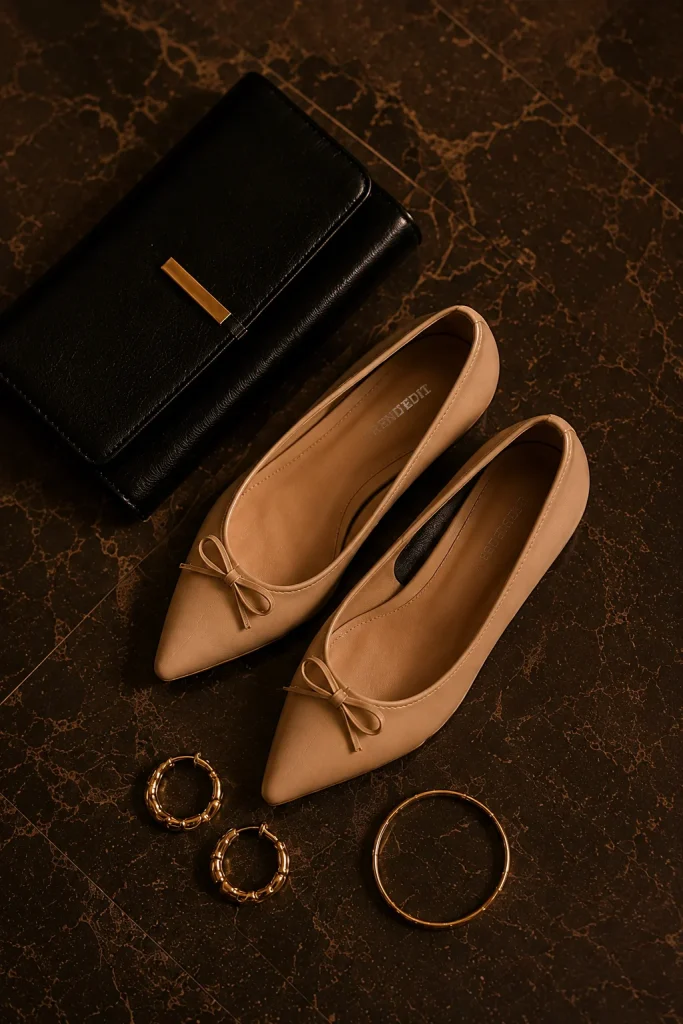 Black clutch, beige flats, and gold accessories on a marble surface.